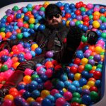 Bearded man in full leather laying in a ball pit